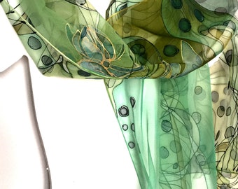 May include: A green silk scarf with a floral and abstract design. The scarf is decorated with black lines, green and gold circles, and a large green flower.