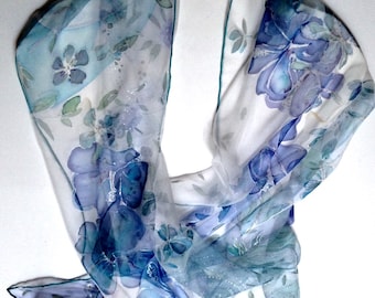 May include: A white silk scarf with a blue and green floral pattern. The scarf has a delicate, flowing design and is perfect for adding a touch of elegance to any outfit.