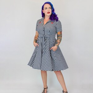 Puede incluir: Un vestido de cuadros vichy blanco y negro con mangas cortas y cintura ajustada. El vestido tiene una falda completa y lo lleva una persona con el pelo morado.