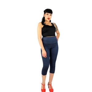 May include: A woman wearing a black cropped top with a sweetheart neckline and dark blue cropped pants. She is wearing red shoes and has her hair styled in a pin-up style.
