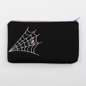 May include: Black zippered pouch with a white embroidered spider web and a pink spider in the center.