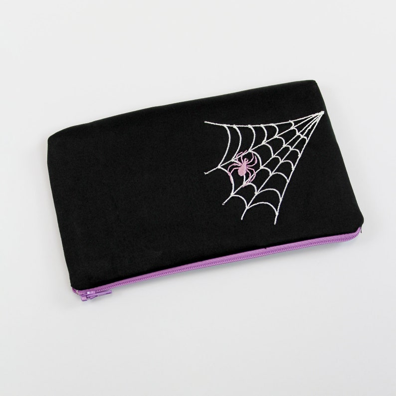 May include: Black zippered pouch with a white embroidered spider web and a pink spider in the center.