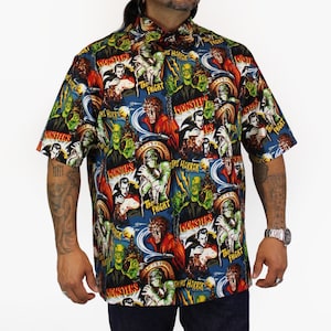 May include: A short-sleeved button-down shirt with a colorful print of classic horror movie posters. The print features images of Frankenstein's monster, Dracula, the Mummy, and the Wolfman. The shirt has a blue background with red, yellow, and green accents.