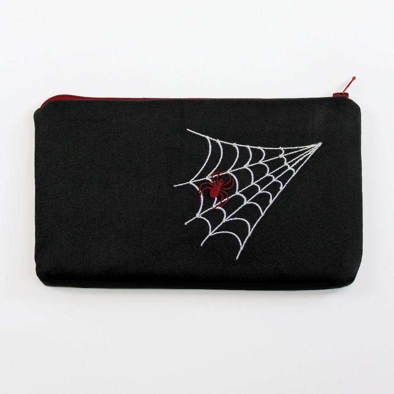 May include: Black zippered pouch with a white embroidered spider web and a red spider in the center.