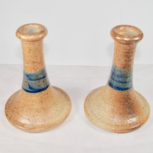 May include: A pair of ceramic candle holders with a brown and tan speckled glaze and a blue stripe around the middle.