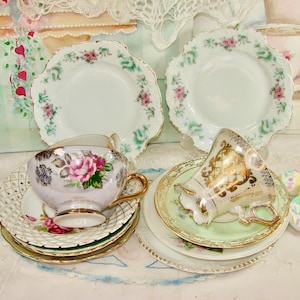 May include: Two vintage teacups and saucers with floral and gold accents. The teacups are on top of a set of three white saucers with gold trim. One saucer has a delicate lace pattern.