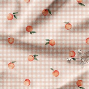 May include: A pink and white gingham fabric with a repeating pattern of peach fruit. The fabric is creased and has a soft, textured look.