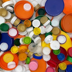 May include: A collection of colorful plastic bottle caps in various sizes and shapes. The caps are in shades of orange, blue, green, white, yellow, and pink. Some caps have a flip-top design, while others are solid.