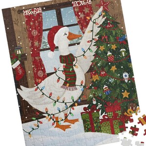 以下が含まれることがあります： サンタ帽とマフラーを身につけ、クリスマスライトで飾られた白いガチョウがクリスマスツリーを飾る、クリスマスをテーマにしたジグソーパズル。雪の降る窓、暖炉、プレゼントが描かれています。いくつかのパズルのピースは分離されています。