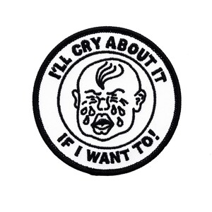 May include: A circular, white embroidered patch with a black border. It features a crying baby illustration in black, surrounded by the text "I'LL CRY ABOUT IT IF I WANT TO!" in black.