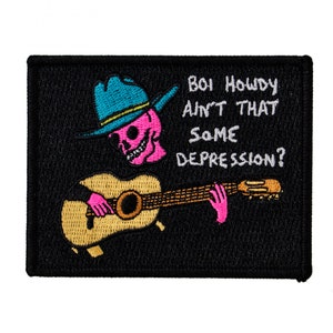 May include: Embroidered patch featuring a pink skeleton wearing a blue cowboy hat and playing a brown acoustic guitar. The text "Boi Howdy Ain't That Some Depression?" is written in white on a black background.