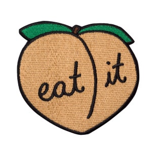 Puede incluir: Un parche bordado con forma de melocotón con el texto "eat it" en hilo negro.