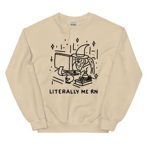 May include: A beige sweatshirt with a black illustration of a wizard sitting at a computer with the text "LITERALLY ME RN".