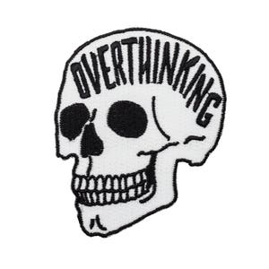 Puede incluir: Parche blanco bordado de una calavera con la palabra "Overthinking" encima.