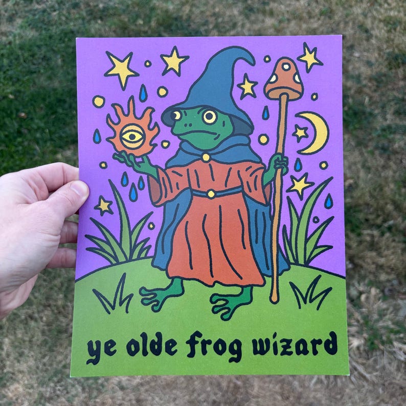 May include: A whimsical illustration of a frog wizard in a blue hat and orange robe, holding a sun with an eye and a mushroom staff. The background is purple with stars, rain, and a crescent moon. The text "ye olde frog wizard" is at the bottom.