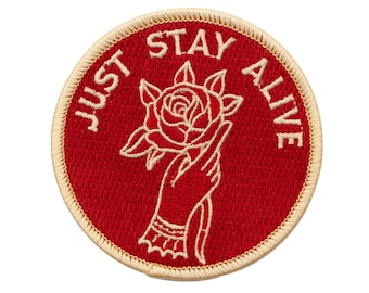 May include: Red embroidered patch with a white outline. The patch features a hand holding a rose with the text "JUST STAY ALIVE" around the image.