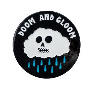 May include: Black enamel pin featuring a white cloud with a skull face and the text "DOOM AND GLOOM" in white letters. Blue raindrops are falling from the cloud.