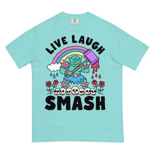 Könnte beinhalten: Hellblaues T-Shirt mit einem Grafikdesign. Es zeigt einen Ork mit Hammer, Regenbogen und den Worten "LIVE LAUGH SMASH". Das Design enthält auch Schädel, Rosen und Regentropfen.
