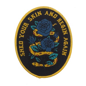 May include: A black embroidered patch with a yellow snake wrapped around two blue roses. The text "Shed Your Skin And Begin Again" is written in a circular pattern around the snake and roses.