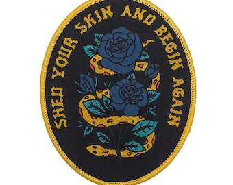 May include: A black embroidered patch with a yellow snake wrapped around two blue roses. The text "Shed Your Skin And Begin Again" is written in a circular pattern around the snake and roses.