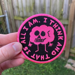 May include: A pink and black embroidered patch featuring a skull-shaped cloud and the text "That's All I Am. I Think And".