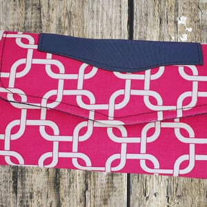 May include: A pink fabric wallet with a white geometric pattern and a navy blue flap. The wallet has a detachable strap with a skull and floral design.