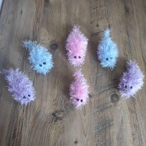 May include: Six fluffy, crocheted cat toys in a variety of colours, including pink, blue, and purple. Each toy has a cute, embroidered face with black eyes and a pink nose.