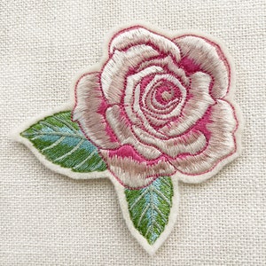 May include: A pink and white embroidered rose with green leaves. The rose is a felt applique.