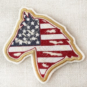 May include: A gold-trimmed embroidered patch shaped like a horse's head with the American flag design. The stars are blue and the stripes are red and white.