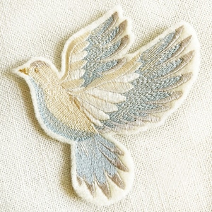 May include: A beige and blue embroidered dove with outstretched wings. The dove is a symbol of peace and hope.