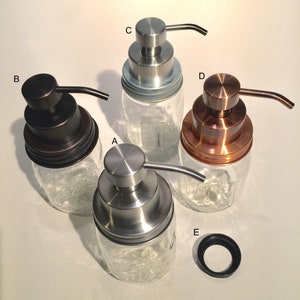 May include: Four glass soap dispensers with different colored tops. The tops are silver, copper, black, and silver. The dispensers are all clear glass and have a pump top.