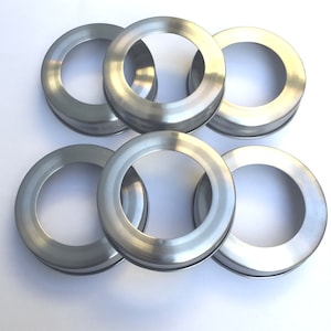 May include: Six silver metal jar lids with a smooth, shiny finish. The lids are stacked on top of each other.