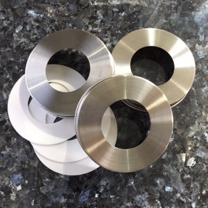 May include: A set of four silver-colored metal rings with a smooth, polished finish. The rings have a circular opening in the center and are stacked on top of each other.