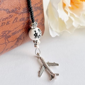 May include: A black and white beaded keychain with a silver airplane charm. The keychain is attached to a brown leather bag.