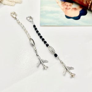 May include: Two silver airplane charm necklaces, one with white beads and one with black beads.