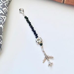 May include: A black beaded keychain with a silver flower charm and a silver airplane charm.