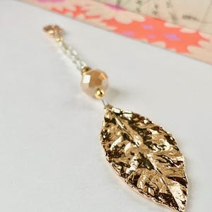 May include: A gold leaf charm pendant with a delicate chain and a clear crystal bead.