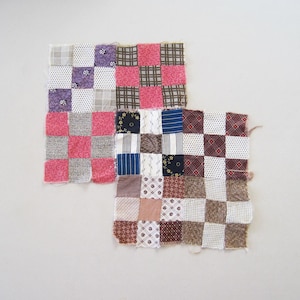 May include: Two handmade patchwork squares with a checkerboard pattern. The squares feature a variety of fabrics in pink, purple, brown, blue, and white. The squares are likely part of a larger quilt or craft project.