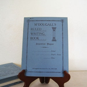 May include: A blue writing book with the title "M'Dougall's Ruled Writing Book" and the words "Superior Paper" printed on the front cover. The book has a decorative border and a small illustration of a column.