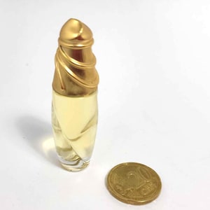 Puede incluir: Un frasco de perfume de vidrio transparente y dorado con un tapón decorativo dorado. El frasco es aproximadamente del tamaño de una moneda de 1 euro.