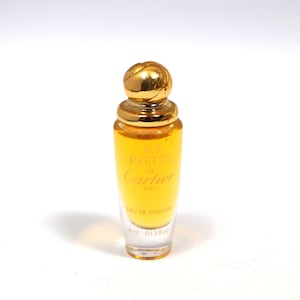 Może przedstawiać: Miniaturowy szklany flakon perfum wypełniony złotym płynem, zwieńczony zaokrągloną nakrętką w kolorze złota. Z przodu znajduje się wyraźny nadruk So Pretty de Cartier Paris Eau de Parfum o pojemności 4 ml oraz 0,13 fl. oz.