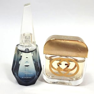 May include: Two perfume bottles. One is a dark blue, geometric bottle with a clear, pointed cap, labeled "Ange ou Démon" by Givenchy. The other is a square bottle with a gold-colored cap and the Gucci logo.