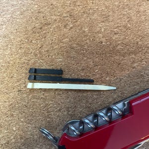 May include: Two small black plastic replacement toothpick accessories and one off-white plastic toothpick accessory positioned above a red multi-tool pocket knife with a visible metal corkscrew and a small metal keyring attachment.