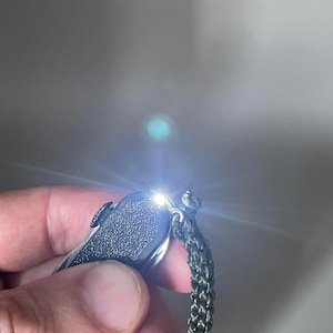 以下が含まれることがあります： テクスチャ加工されたハンドルを持つ黒いマルチツールポケットナイフ。上部から明るい白色LEDライトが発光しています。オリーブグリーンの編み込みパラコードストラップが、金属仕上げのツールの端にある金属リングに取り付けられています。