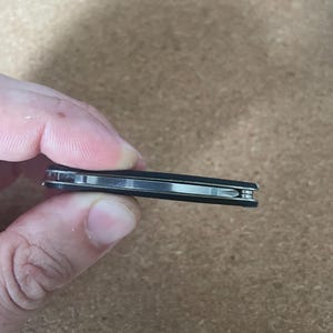 Peut inclure: Un multi-outil fermé et fin doté d'un manche noir mat et d'un mécanisme intérieur en acier inoxydable visible. L'outil est de forme rectangulaire avec des bords arrondis, présentant un design compact avec une finition métallique sur le profil.