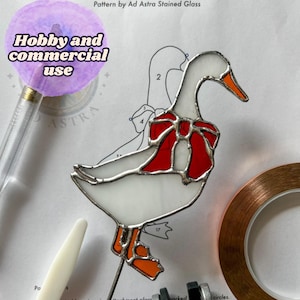 Puede incluir: Un patrón de atrapasol de vidrio coloreado con una oca con un lazo rojo, piezas numeradas y cinta de cobre. El patrón es para uso de hobby y comercial.