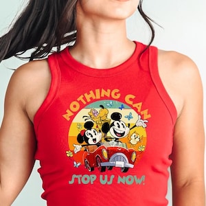 May include: Red tank top with a graphic featuring Mickey and Minnie Mouse in a red car, with the text "NOTHING CAN STOP US NOW!". The design is set against a yellow, orange, and red background.