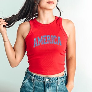 a woman in a red tank top is holding her hair
