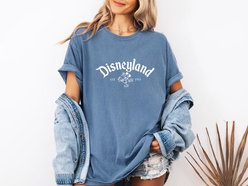 a woman wearing a disneyland shirt and denim shorts