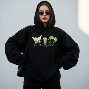 May include: Black hooded sweatshirt with a front pocket and a graphic featuring a fairy, a bow, and the text "Fly with faith and trust." The fairy is wearing a green dress and has blonde hair. The bow is green and white.